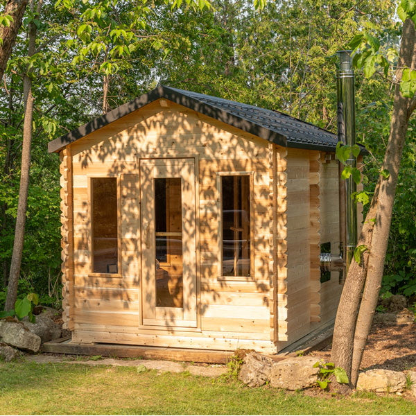 A small Dundalk Canadian Timber CT Georgian Cabin Sauna with Changing Room made of Eastern White Cedar in a wooded area.