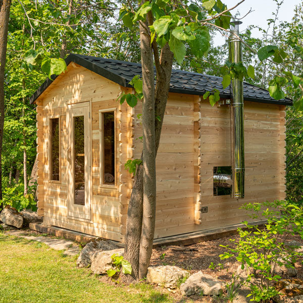 An Eastern White Cedar Dundalk Canadian Timber CT Georgian Cabin Sauna with Changing Room tucked away in the woods, offering a tranquil sanctuary for those seeking a cozy and rustic getaway. (Brand Name: Dundalk LeisureCraft)