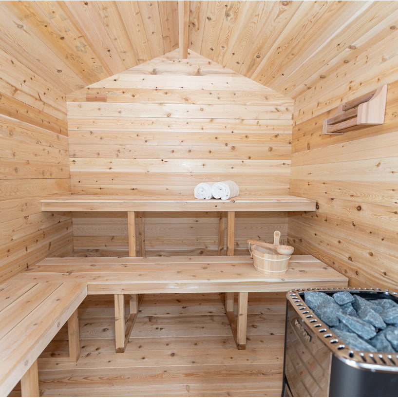 A luxurious backyard sauna made of Eastern White Cedar, complete with benches and a wood stove. This stunning space, reminiscent of a Dundalk Canadian Timber Georgian Cabin Sauna by Dundalk LeisureCraft, offers the perfect retreat for relaxation and recovery.