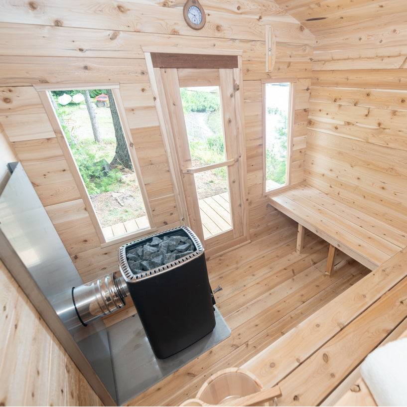 A luxurious Dundalk Canadian Timber Georgian Cabin Sauna nestled in a backyard, featuring a stove, window, and Eastern White Cedar accents. Perfect for creating a serene recovery space.