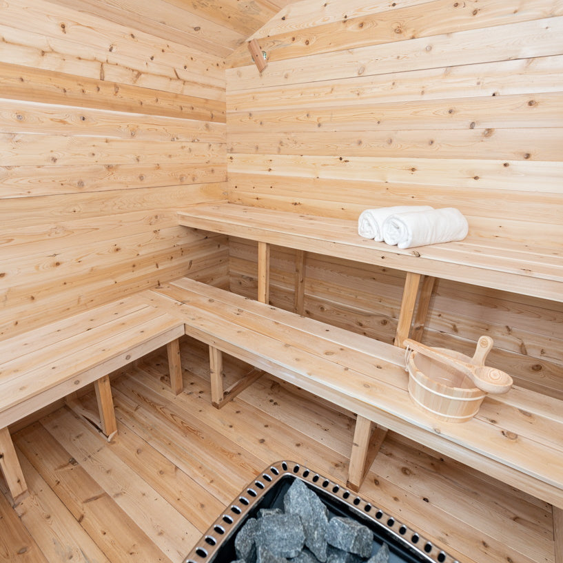 A luxurious Dundalk Canadian Timber Georgian Cabin Sauna made of Eastern White Cedar, providing a tranquil backyard recovery space with a bench and rock.