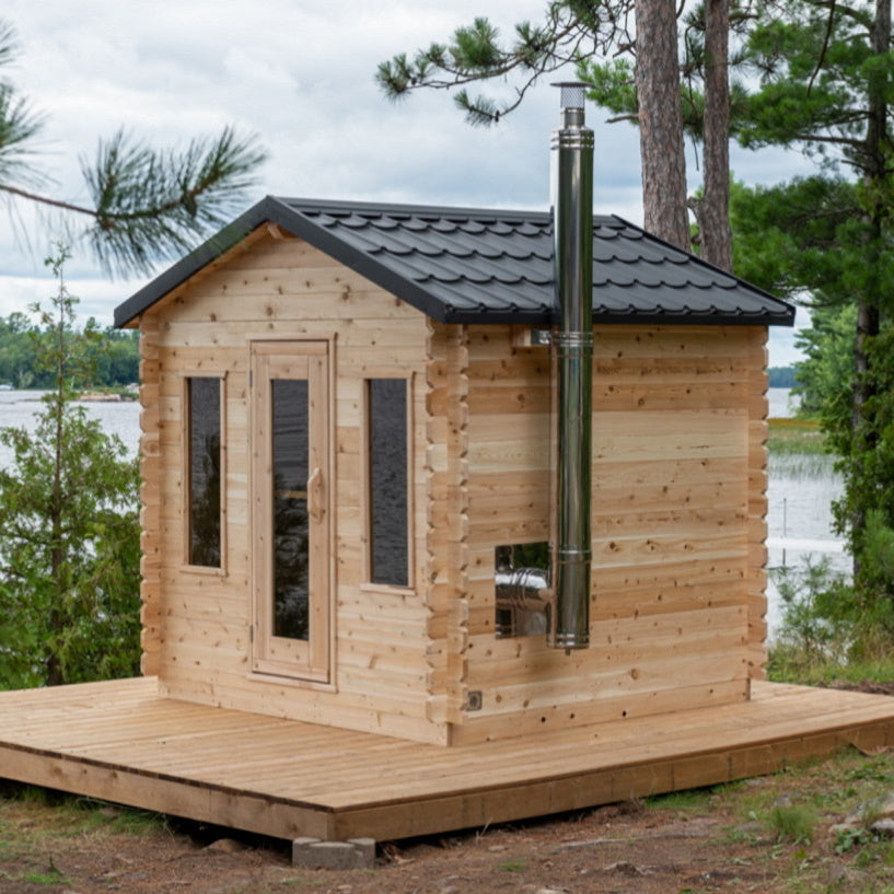 A Dundalk Canadian Timber Georgian Cabin Sauna made of Eastern White Cedar sitting on a wooden deck next to a lake.